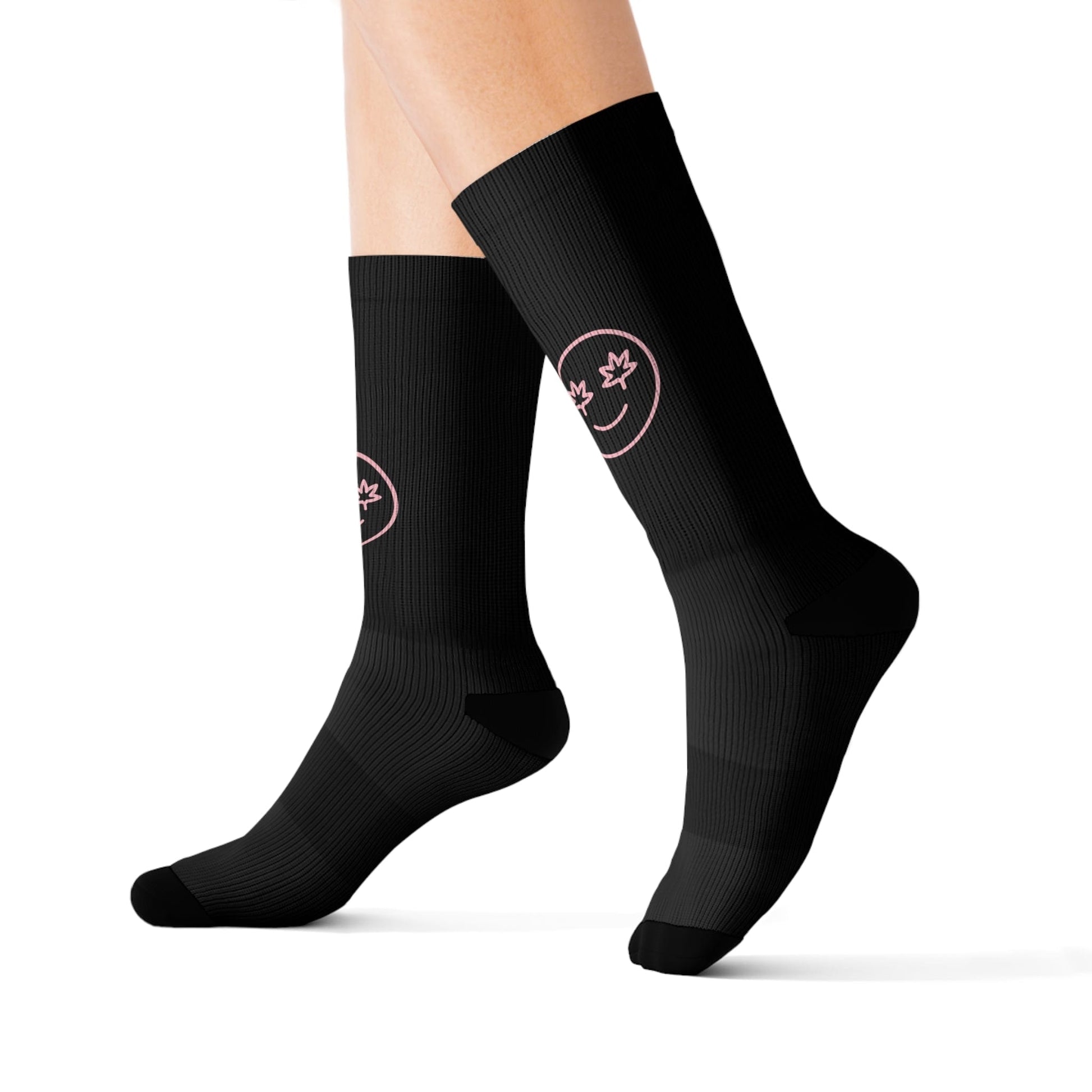 A person wears High Stepper Weed Socks—black crew socks with a pink smiley face and a maple leaf design on the calf of each sock.