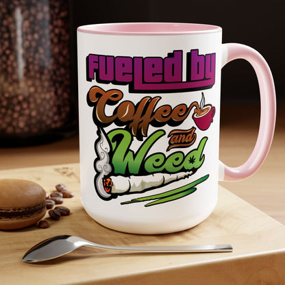 The Fueled by Coffee and Weed 15oz Coffee Mug is a white ceramic mug with pink accents, featuring "Fueled by Coffee and Weed" with coffee cup and joint graphics. Nearby are a spoon, coffee beans, and a macaron.