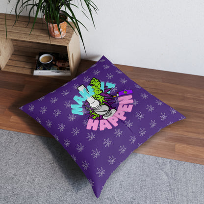 A purple Make It Happen Cannabis tufted floor pillow, square with a "make it happen" graphic in vibrant colors, placed on a wooden floor next to a plant and a cup.