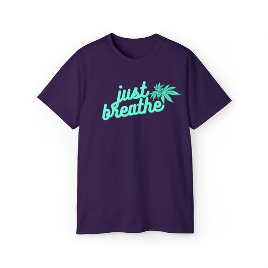 A purple T-shirt with the phrase "Just Breathe" and an illustration of a cannabis leaf printed in light blue on the front. This Just Breathe Cannabis Tee exudes relaxation with its soothing design.