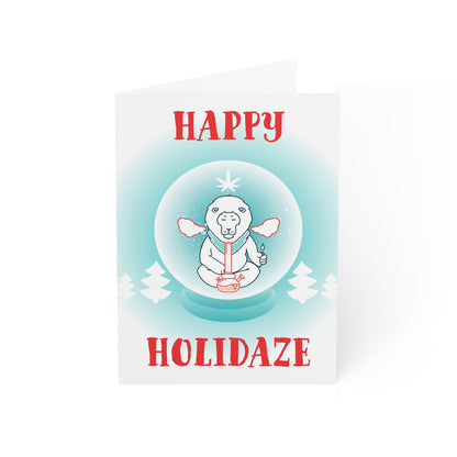 A Happy Holidaze Zen Lion Smoking Bong Merry Christmas card featuring a cartoon polar bear meditating inside a snow globe, crafted from sustainable paper, with the text "happy holidaze" above and below the globe.