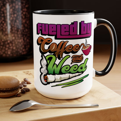 The Fueled by Coffee and Weed 15oz Coffee Mug, featuring a coffee cup and rolled joint graphic with the phrase "Fueled by Coffee and Weed," sits on a wooden surface beside a spoon and macaron.