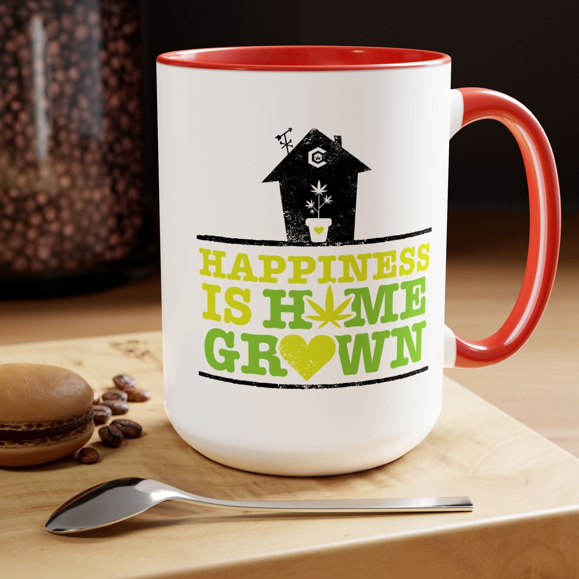 On a wooden surface, next to a spoon, coffee beans, and a macaron, sits the Happiness Is Homegrown Weed Coffee Mug