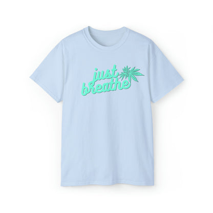 Light blue T-shirt with the words "just breathe" in green text and a green cannabis leaf graphic. This Just Breathe Cannabis Tee offers a perfect blend of relaxation and style with its soothing message and distinctive cannabis leaf design.