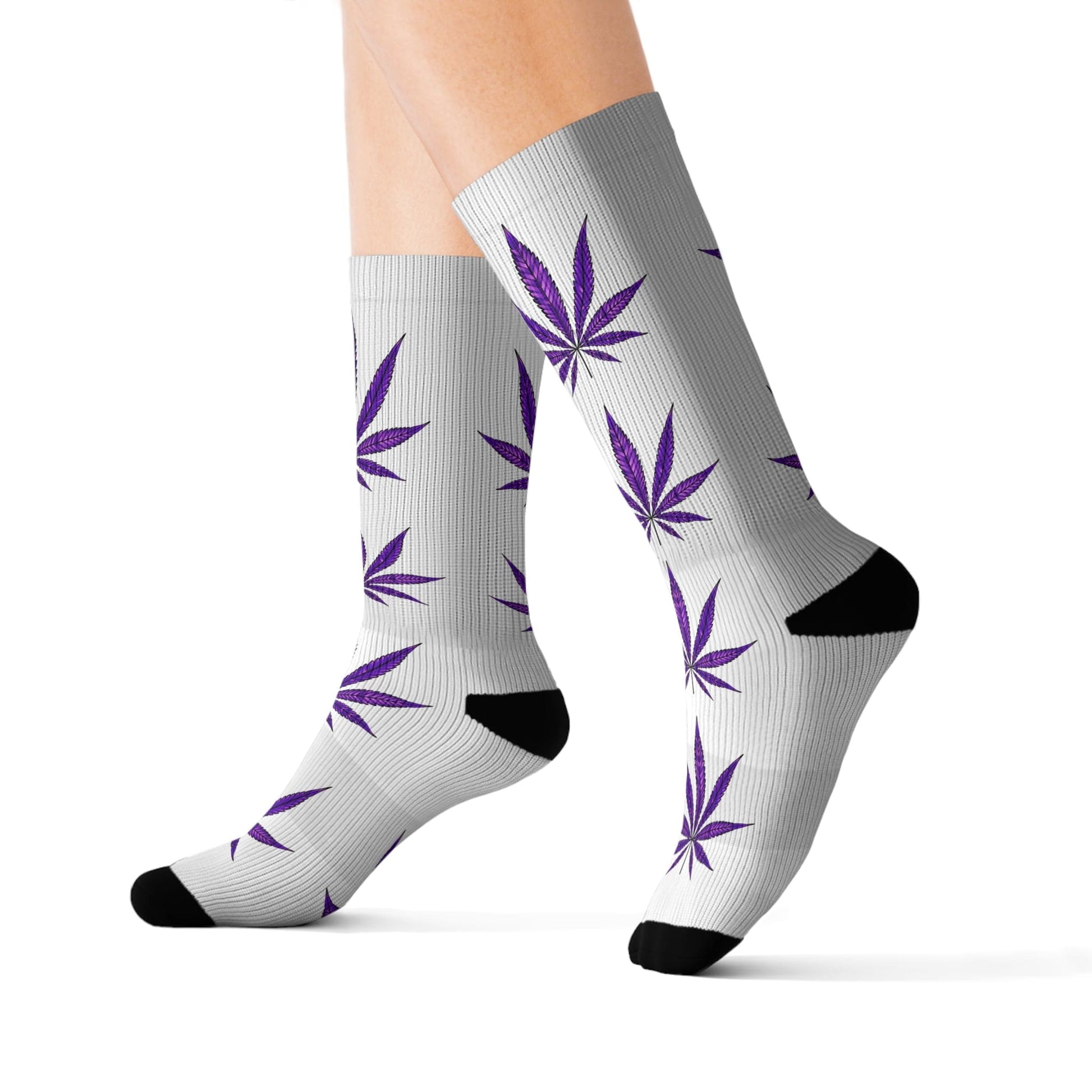 A person wears Purple Haze Weed Socks—gray crew socks with black toes and heels, featuring a purple cannabis leaf pattern—while standing on a white background.