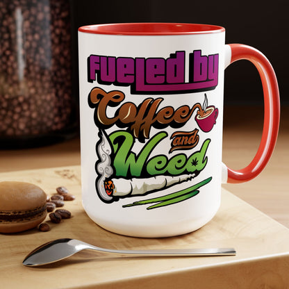 The Fueled by Coffee and Weed 15oz Coffee Mug rests on a wooden surface, accompanied by a spoon, coffee beans, and a macaron.