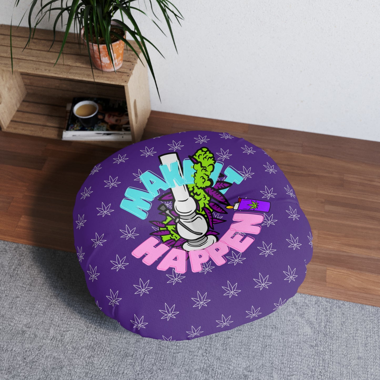 A round purple Make It Happen Cannabis, Bong, & Lighter custom floor pillow with a colorful design featuring the text "make it happen" and an illustration of a hand holding a smoking joint, placed on a wooden floor near a shelf with a plant