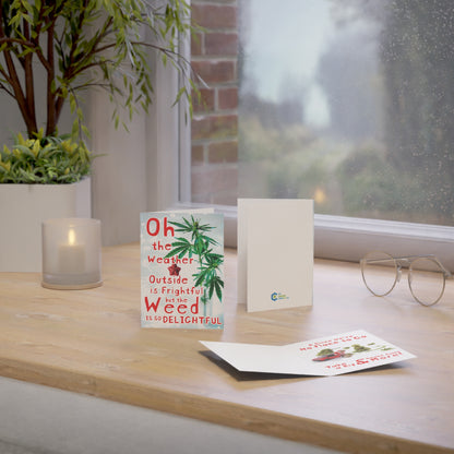 A cozy indoor setting with a Weed is So Delightful Greeting Card, candles, glasses, and a plant on a wooden table near a window with a rainy view.