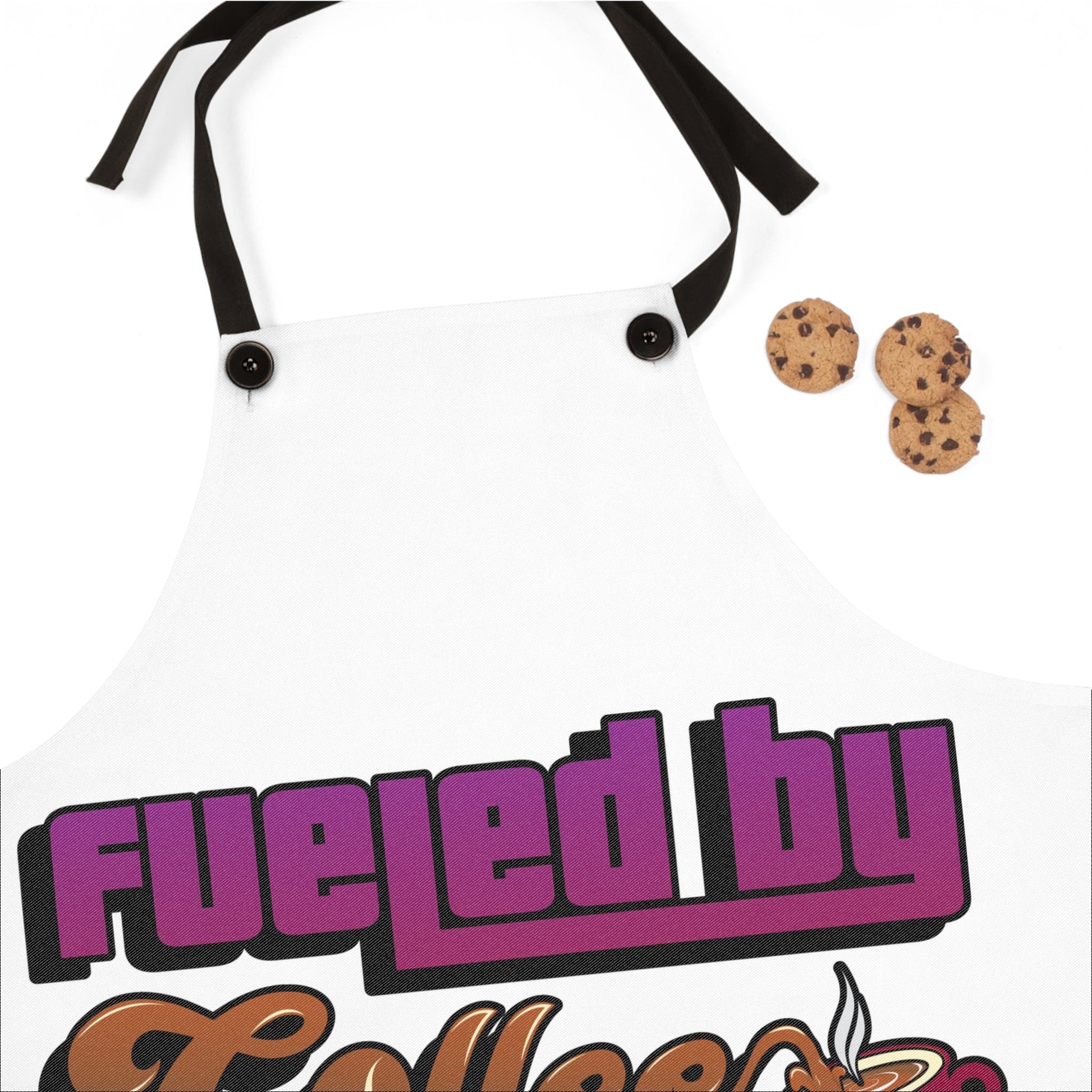 A white personalized "Fueled by Coffee and Weed" apron with black straps features bold, colorful text, displayed on a white surface next to three chocolate chip cookies.