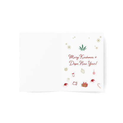 Mary Kushmas + Dope New Year Marijuana Tree Christmas Greeting Cards open on a flat surface, featuring a cannabis leaf design and the text "merry juana and dope new year!" on FSC certified paper, surrounded by holiday-themed doodles.