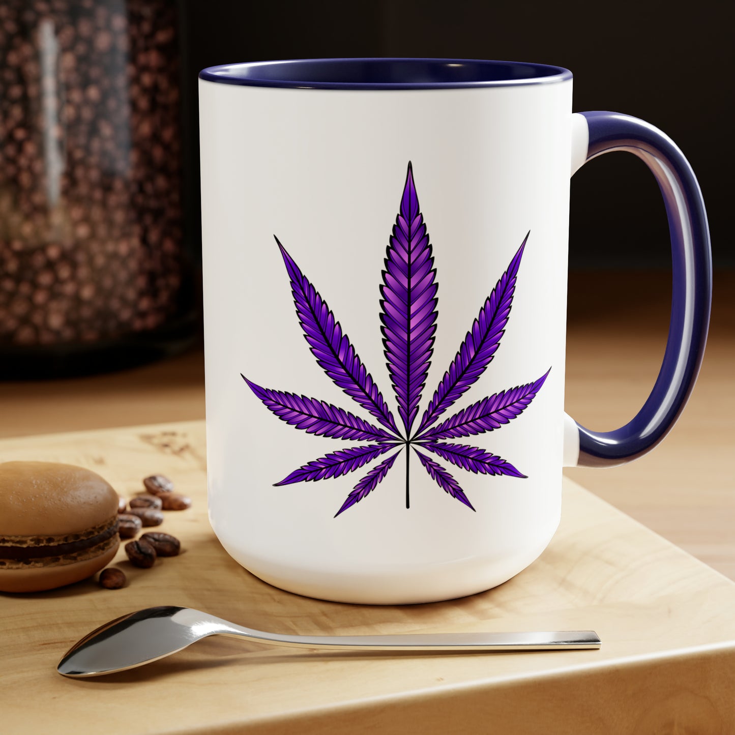 Purple Haze Marijuana Coffee Mug on a wooden table featuring a Purple Haze Marijuana leaf design, accompanied by coffee beans, a spoon, and a macaron.