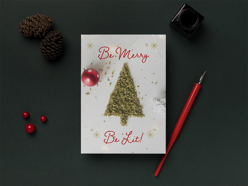 Stoner Christmas card with ground cannabis in the shape of a tree. There is a red ornament and gold illustrated snowflakes. The background has pine cones, ink pen with ink jar.