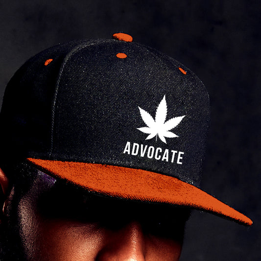 Close up photo of a young man wearing an orange and black pot leaf hat with a white marijuana leaf on the front center with the word "Advocate" written beneath it