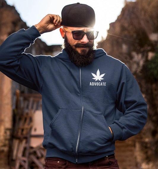 A person with a beard and sunglasses, wearing the blue Cannabis Advocate Weed Zip Up Hoodie featuring a leaf and the word "Advocate" printed on it, adjusting their baseball cap while standing outdoors.