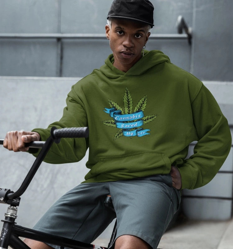 A person wearing a Cannabis Saved My Life Marijuana Hoodie with a green cannabis leaf design sits on a bicycle, radiating healing vibes and representing the cannabis community.