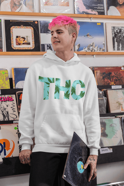 A person with pink hair wears a stylish THC Mens Weed Hoodie while browsing a record store, holding onto a vinyl record.