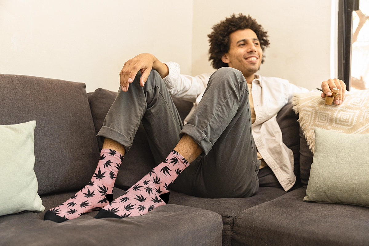 Man sitting on the couch wearing Pink Stoner socks smoking a pipe