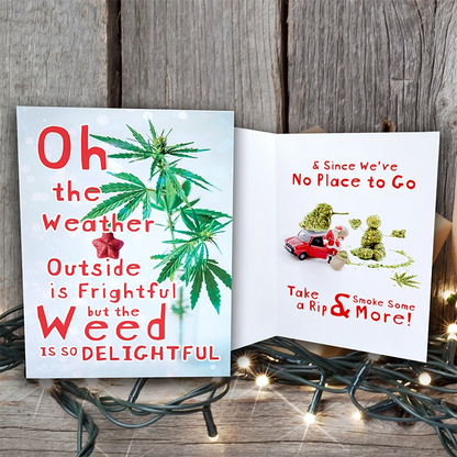 A whimsical "Weed is So Delightful" holiday card open on a wooden surface, featuring a marijuana leaf and playful text about weather and smoking weed, surrounded by twinkling lights. This greeting card is one of our customized greeting cards.