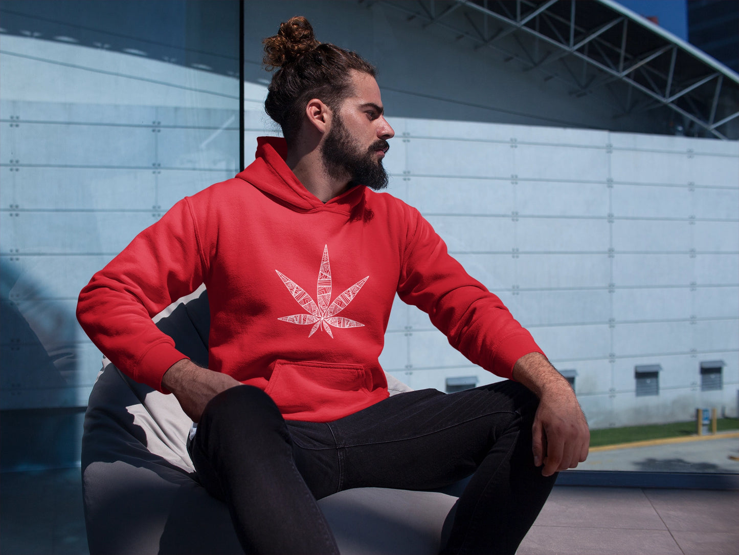 Man with hair bun sitting on beanbag chair wearing a red tribal cannabis leaf red hoodie