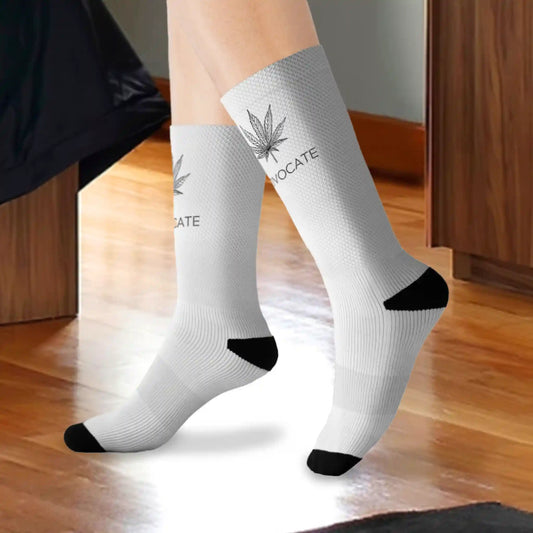 A closeup of a person wearing black and white weed socks that show a cannabis leaf on the top front of the sock with the words that read "advocate" in a bedroom