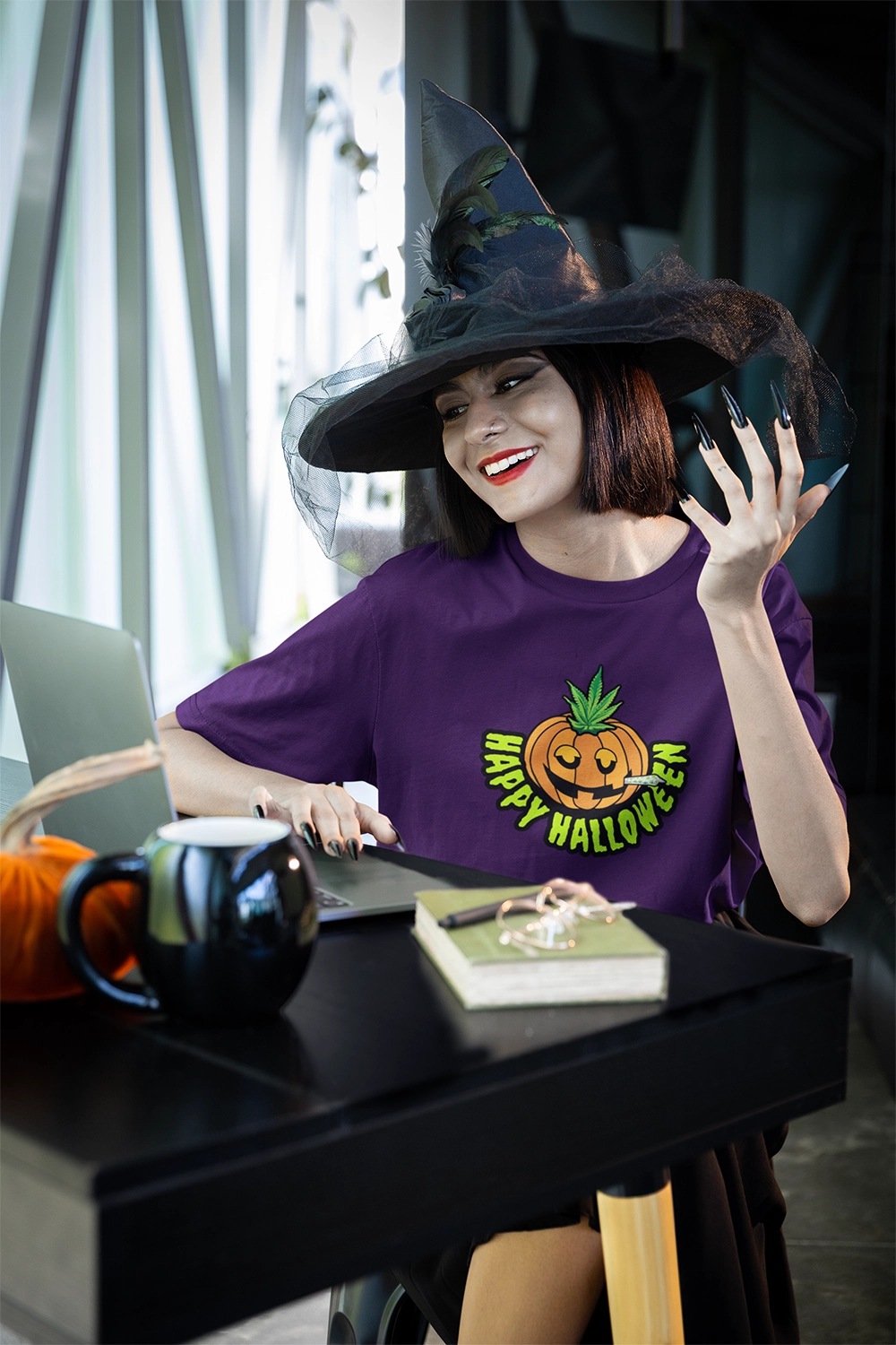 Witch sitting at desk wearing a purple Happy Halloween Pumpkin Stoner Weed Shirt
