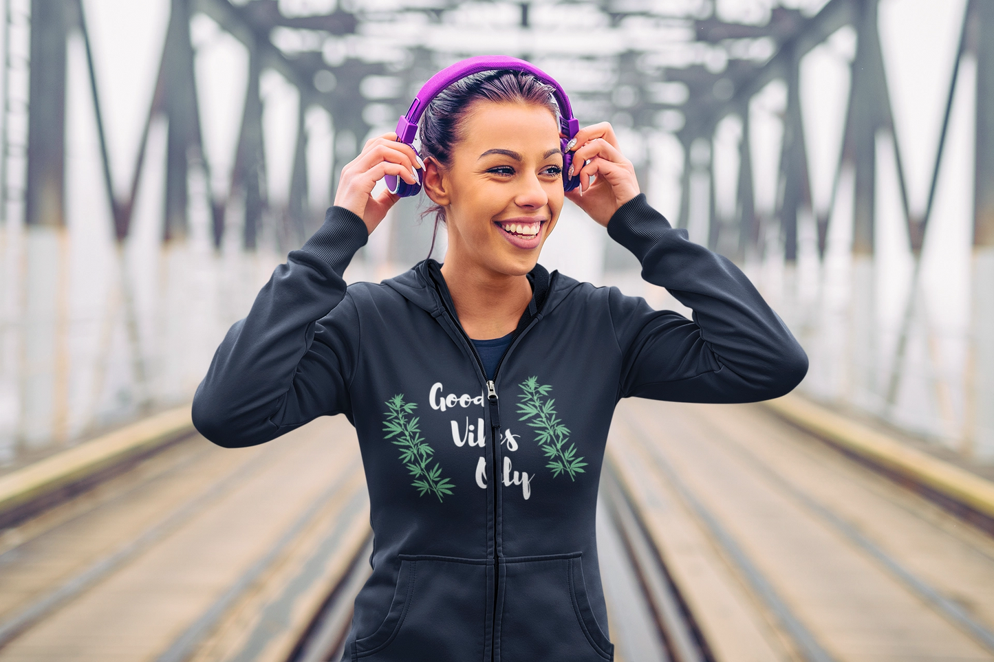 A young woman is wearing a navy blue good vibes only weed zip up hoodie while wearing a pair of purple headphones.