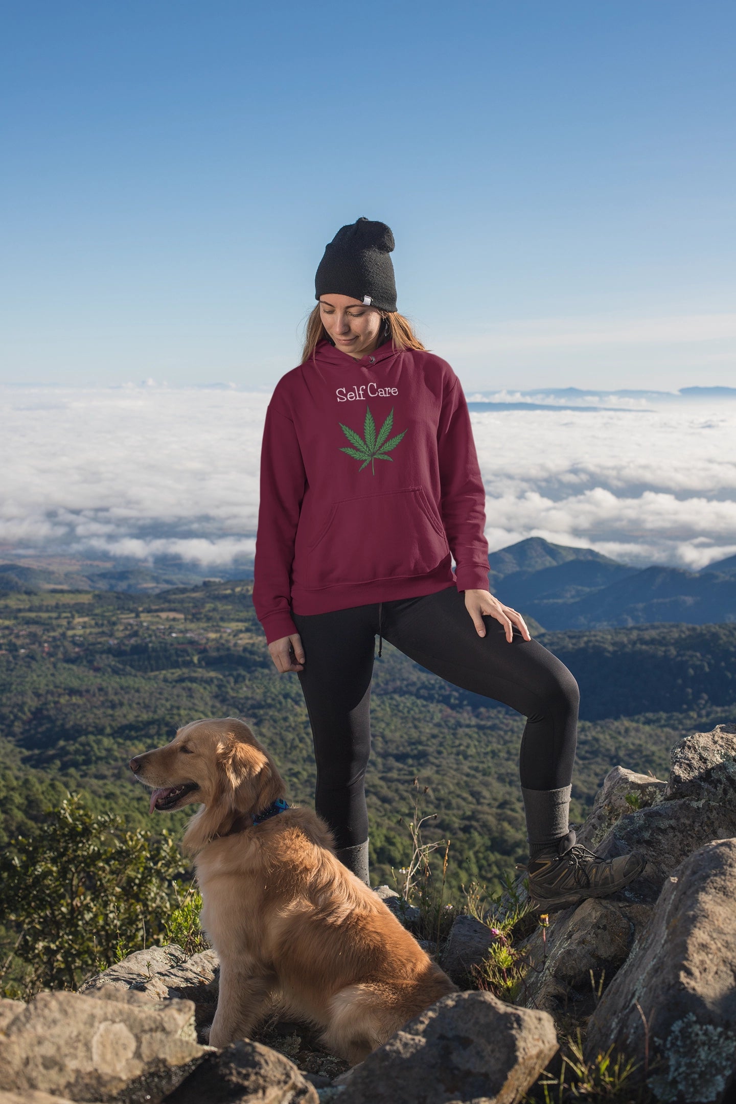Woman with her dog hiking mountains wearing a maroon Self Care Marijuana Hoodie