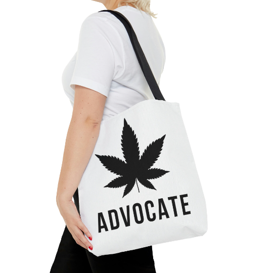 A woman wearing the Cannabis Advocate Pot Leaf | Beach Grocery Tote Bag with huge black weed leaf in the center of the bag and the word Advocate boldly written beneath