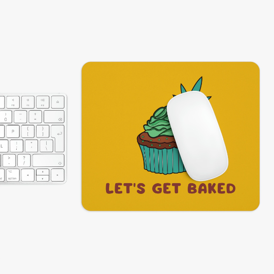 A computer setup with a white keyboard and a mouse on a Let's Get Baked Marijuana Yellow Mouse Pad featuring a cartoon cupcake and the phrase "let's get baked.