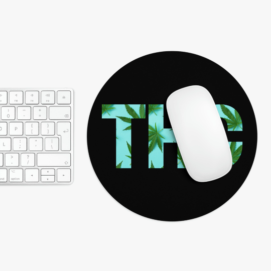 White computer mouse on a round THC Marijuana Black Mouse Pad with a cannabis leaf design, next to a white keyboard on a white surface.