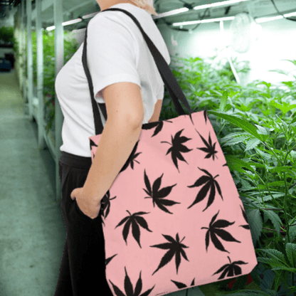 Person with a Marijuana Leaves Pink Tote Bag is standing in a greenhouse surrounded by rows of plants.