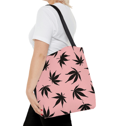 Person carrying the Marijuana Leaves Pink Tote Bag, which is adorned with black leaf patterns, while dressed in a white t-shirt and black pants.