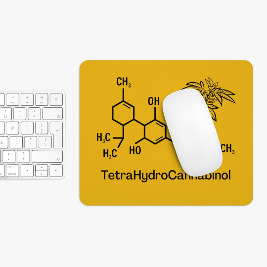 A white mouse on a THC Yellow Mouse Pad featuring the chemical structure of Tetrahydrocannabinol and a small cannabis leaf graphic, next to a white keyboard on a desk.