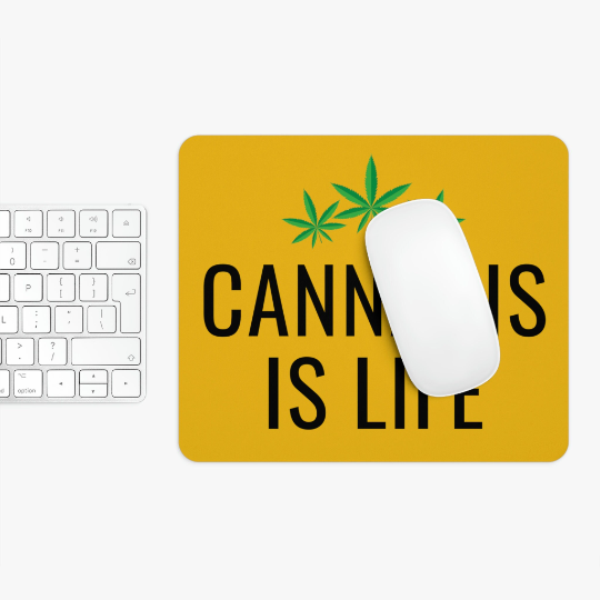 A white computer mouse on a Cannabis is Life Yellow Mouse Pad with "cannabis is life" text and cannabis leaf design, next to a white keyboard on a white surface.