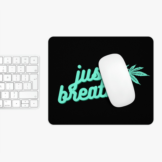 A white computer mouse on a Just Breathe Cannabis Black Mouse Pad with "just breathe" in neon green text, next to a white keyboard on a white surface.