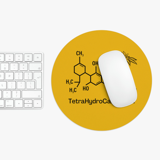 White computer mouse and keyboard on a white surface beside a round Tetrahydrocannabinol (THC) Yellow Mouse Pad featuring a THG chemical structure diagram labeled "tetrahydrocannabinol.