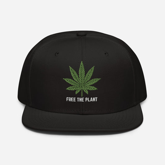 Black Free The Plant snapback baseball cap featuring a green cannabis leaf design and the phrase "free the plant" embroidered in white.