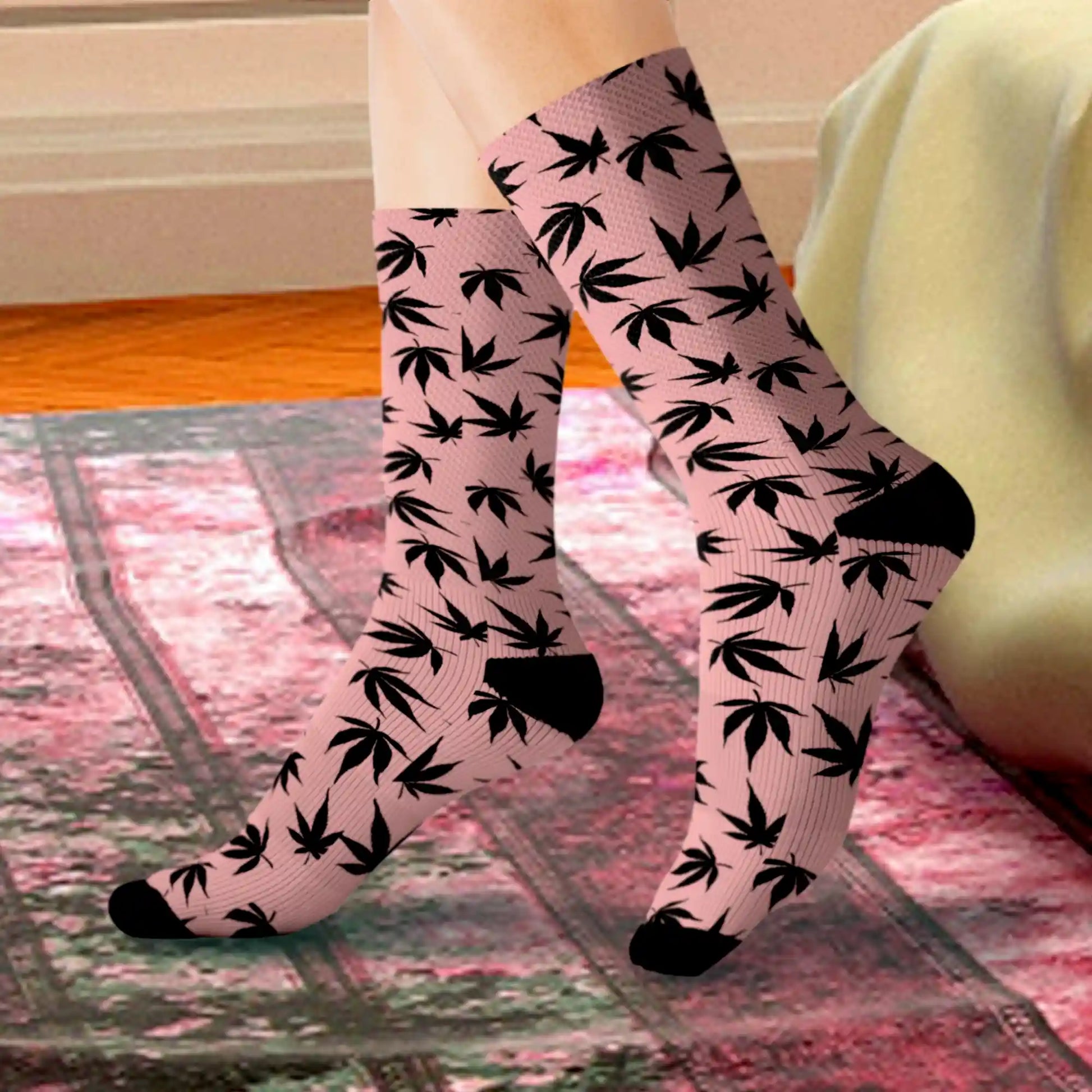 a close up of a stylish pair of pink and black marijuana socks with black cannabis leaves all over in a bedroom setting