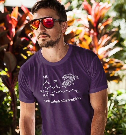 A man with a beard and sunglasses stands outdoors wearing a purple Tetrahydrocannabinol (THC) Molecule Weed Shirt displaying the chemical structure and name of TetraHydroCannabinol. Red foliage is visible in the background.