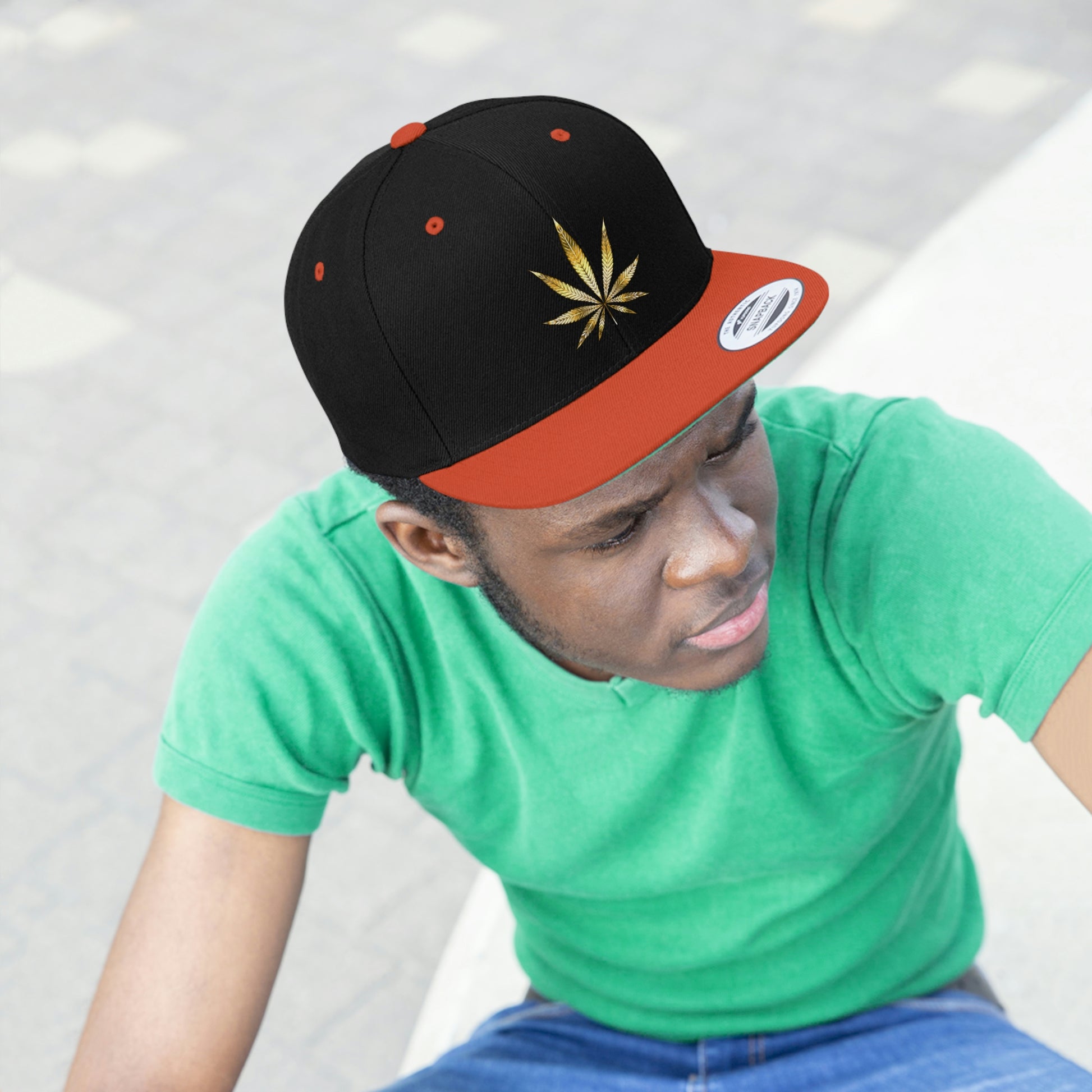 Picture of a young man watching curiously in a green t shirt with the orange and black Gold Marijuana Leaf Snapback Hat