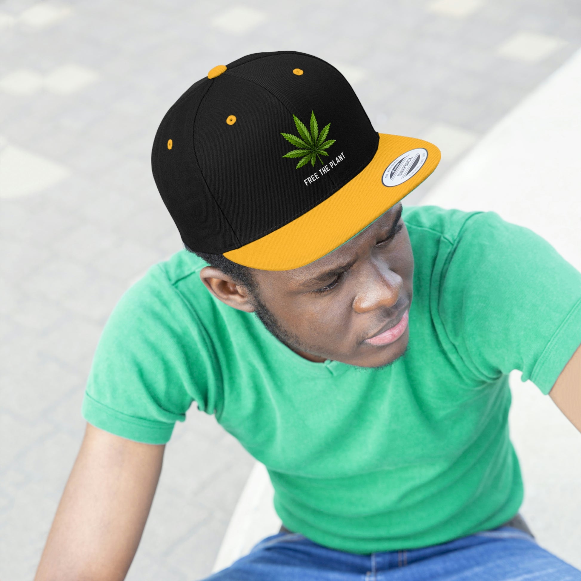 A young man looks awesome with the gold and black Free The Plant Marijuana Snapback Hat with green cannabis leaves a green underbill and a matching green t-shirt