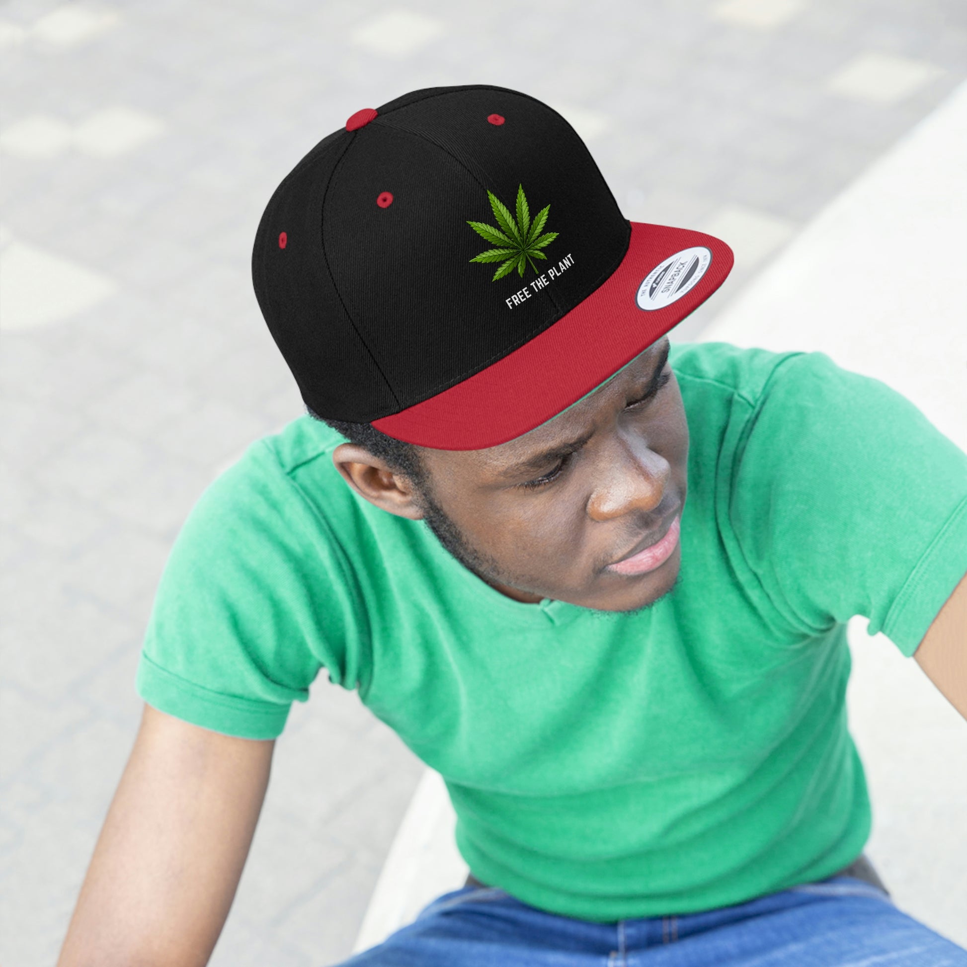 A young man looks cool with the red and black Free The Plant Snapback Hat with green a cannabis leaf a green underbill and a matching green t-shirt