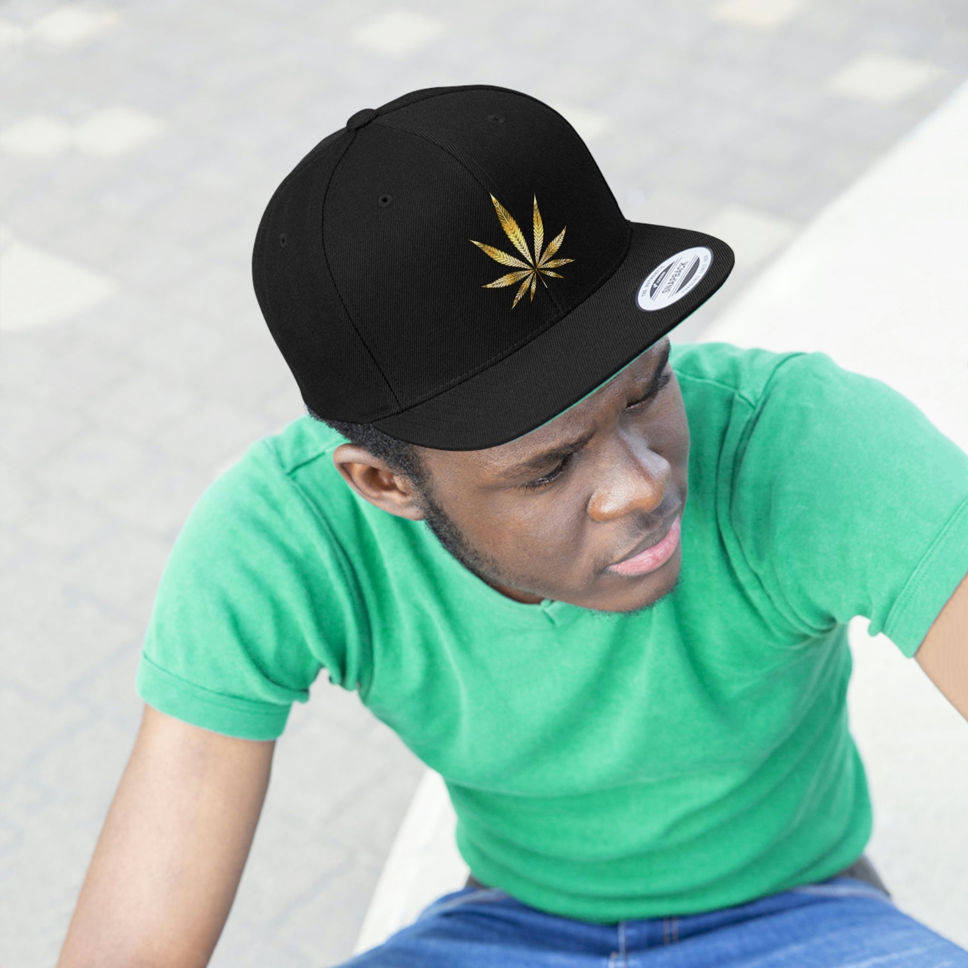 Picture of a young man watching intently in a green t shirt with the all black Gold Marijuana Leaf Snapback Hat