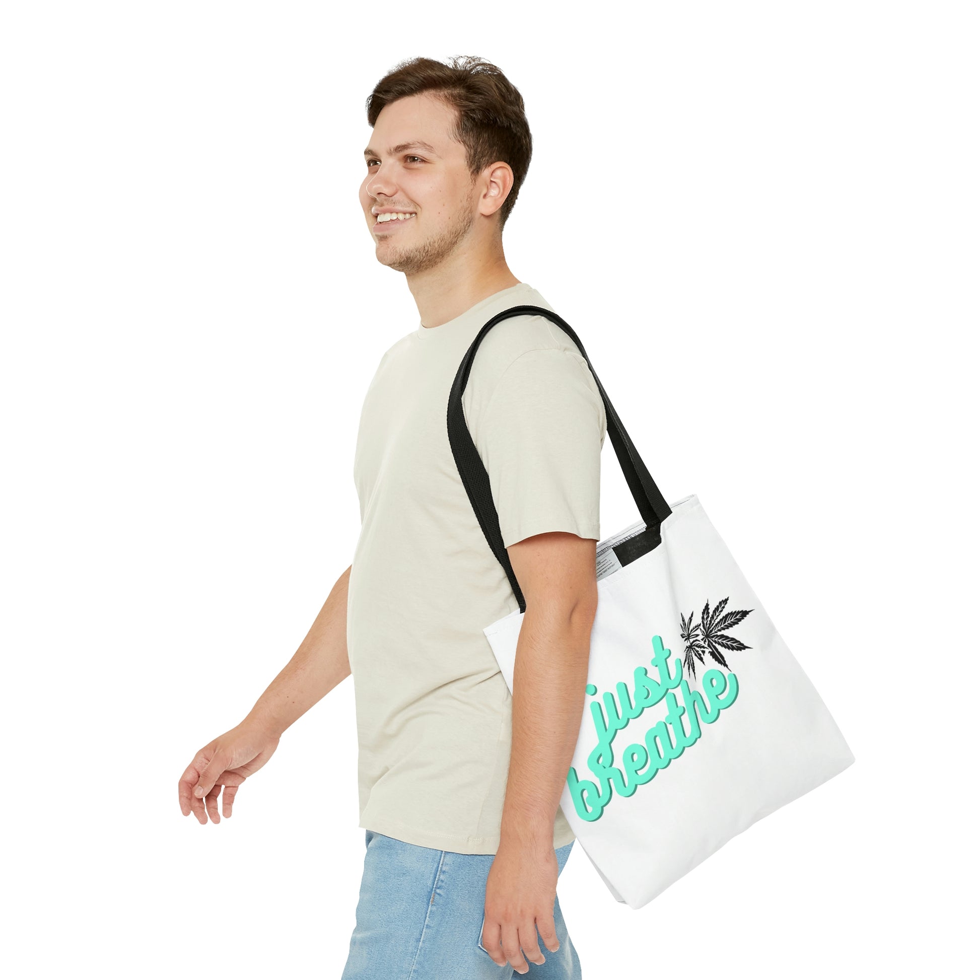 A man with short hair and jeans is walking with hands out front while carrying the Just Breathe Cannabis Tote Bag over his shoulder 