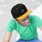 Photo of a young man looking as he wears the black and gold  Rainbow Marijuana Leaf Snapback Hat
