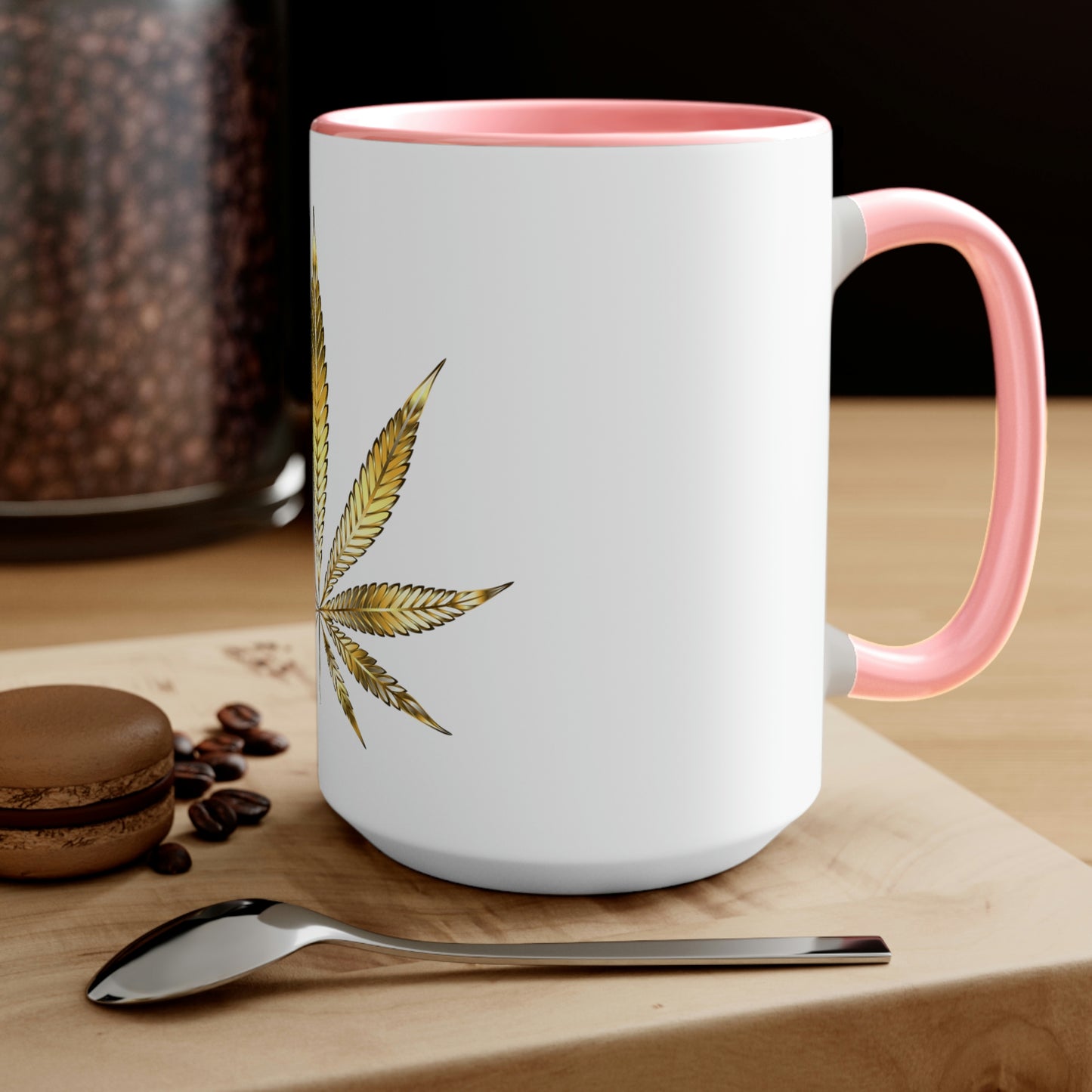 A white cannabis mug with a pink interior featuring a bright gold weed leaf on the front center, sitting on a wood base.