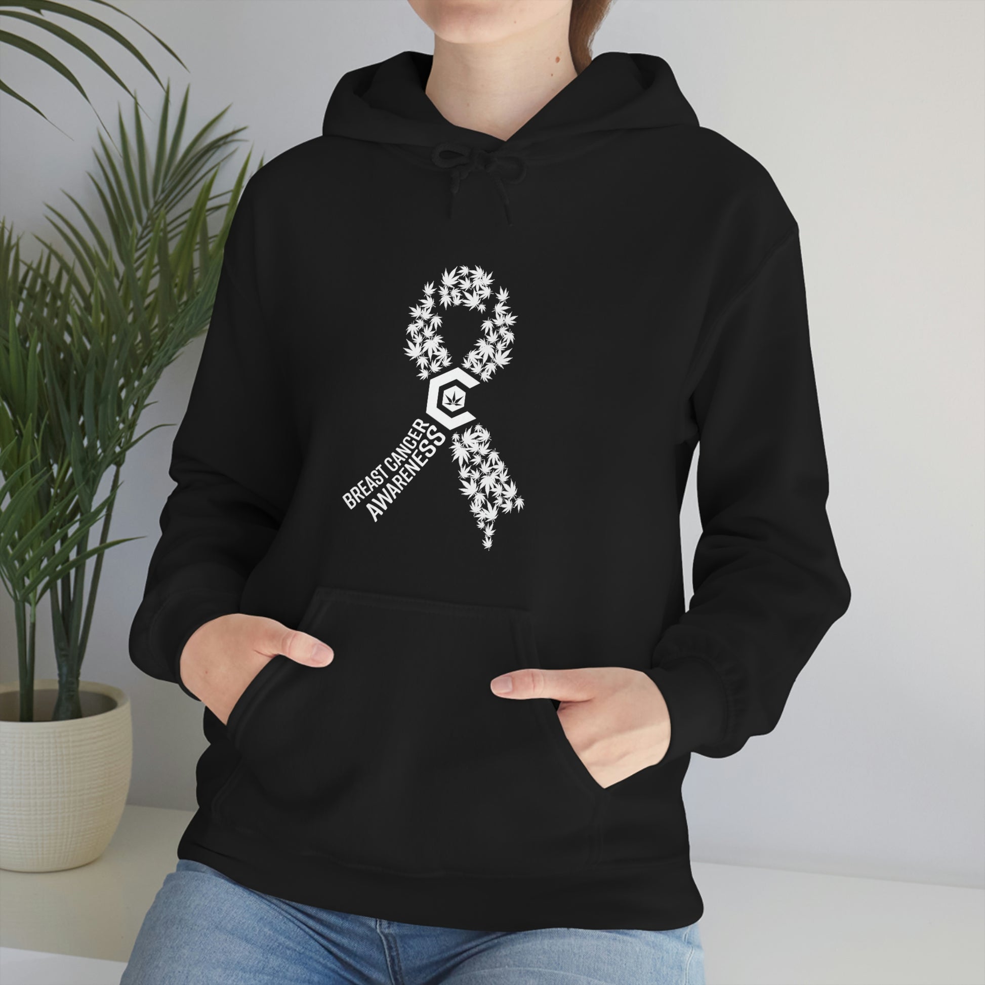 A woman wearing a Breast Cancer Awareness Cannabis Pullover Hoodie with a white ribbon on it.