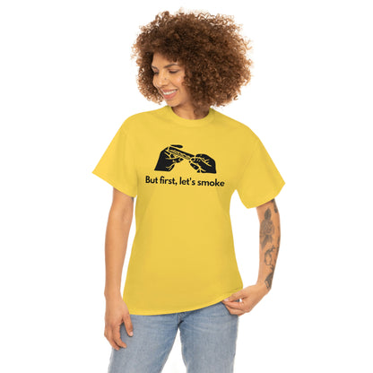 A young woman wearing a yellow cotton t-shirt that reads "but first, let's smoke" and shows a pair of hands in black silhouette rolling a weed joint