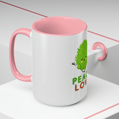 a Cannabis, Peace and Love Coffee Mug with a green leaf on it and a pink handle.