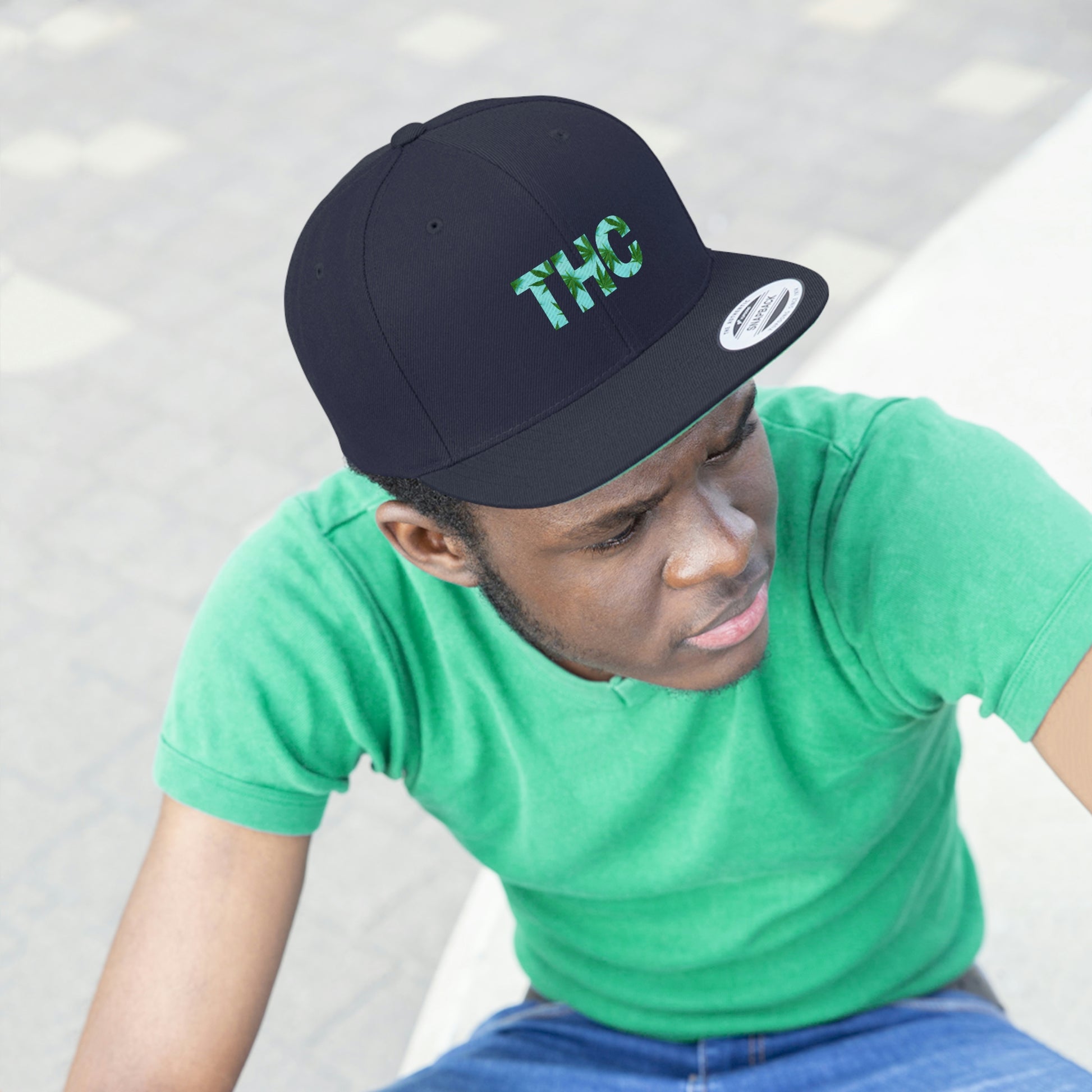 Navy blue THC Snapback Hat with mellow green background while the letters THC are infused with cannabis leaves being worn by a young man looking onward 